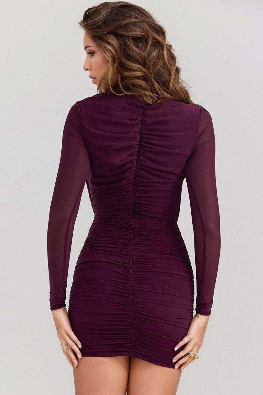 Woman wearing a burgundy ruched dress against a plain background